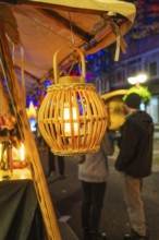 A warm lantern illuminates a night market stall, people stand in the background, Feuernacht,