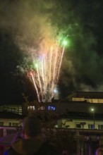 Colourful fireworks light up the night sky, smoke drifts through the air and people watch