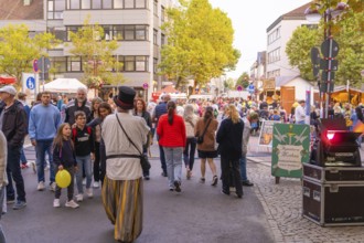 Crowds at a street festival, children with balloons and colourful stalls in an urban environment,