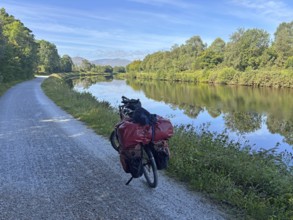 A loaded bike ride along a river under clear skies and lush vegetation, Caledonian Canal, Fort