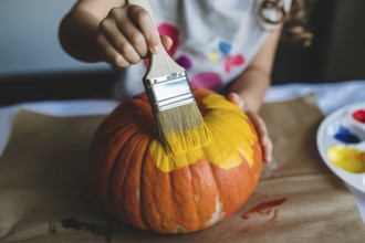 Close up of orange Halloween pumpkin being painted yellow by a child, AI generated
