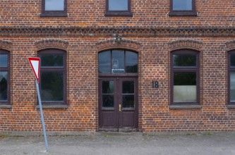View of the entrance area of a brick building with a leaning traffic sign in front of it, Uenzen,