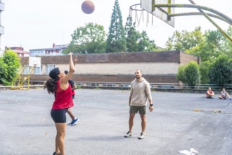 Young woman practicing basketball shooting at the hoop under the supervision of her coach on an