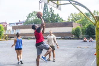 Group of friends enjoying a game of basketball on an outdoor court, with a young man shooting the