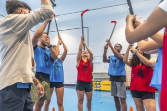 Group of floor hockey players wearing colorful uniforms raising their sticks together in