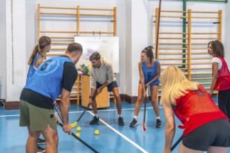 Floorball team practicing game strategy with their coach in a gymnasium, focusing on teamwork and