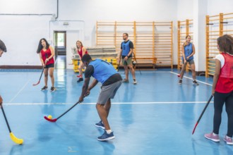 Floorball team players practicing passes during training inside a gym, skillfully hitting the ball
