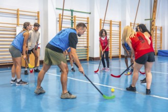 Two floorball teams wearing colorful sportswear are practicing passes and shots in a gymnasium,