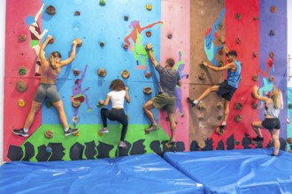 Five athletes climbing a bouldering wall in a gym, focusing on their training and exercising