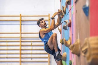 Young male athlete practicing sport climbing on a colorful indoor climbing wall, demonstrating