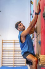Concentrated male athlete meticulously gripping colorful handholds while ascending an artificial