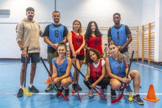Multi ethnic floorball team posing together with their sticks in gymnasium after training session,