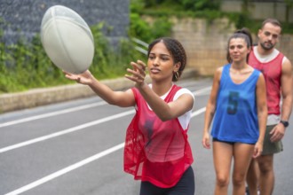 Young woman wearing a red training bib practices passing a rugby ball on a sports field, while