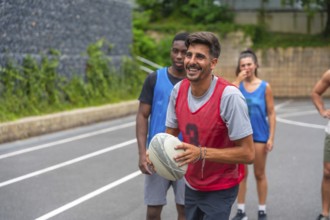 Rugby player wearing a red training bib smiling while holding the ball during a lively training