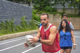 Male rugby player wearing red training bib holding and passing rugby ball on outdoor court during