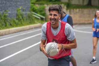 Male rugby player wearing a red training bib smiles broadly while holding the ball during practice