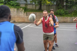 Group of athletes passing a rugby ball during a training session on an urban basketball court,