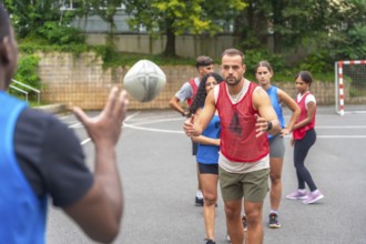 Multi ethnic rugby players engaging in passing drills on an outdoor court within a city park,