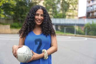 Young woman wearing a blue rugby uniform, confidently holding a rugby ball while smiling on an