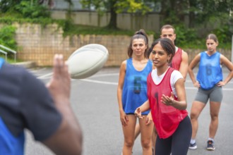 Coach throws a rugby ball to a group of female players wearing numbered jerseys during a training
