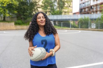 Female rugby player wearing a blue shirt, smiling confidently while holding a rugby ball on an