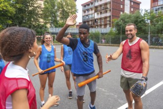 Group of cheerful multi ethnic friends wearing sportswear giving high fives and holding bats while