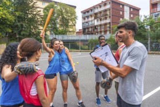 Female baseball players celebrating a victory with their coach holding a clipboard, discussing