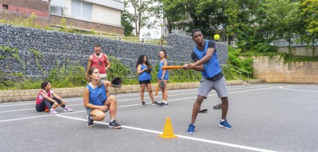 Multi ethnic baseball players practicing on an urban field, with a batter hitting the ball and a