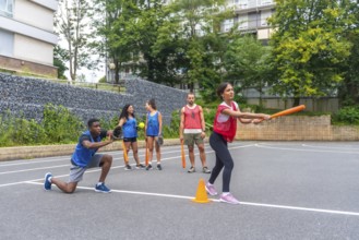Group of friends enjoying a lively game of baseball on an outdoor court, with a woman swinging an