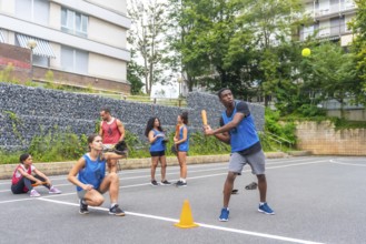 Group of young friends playing baseball in an urban environment, with a male player hitting the