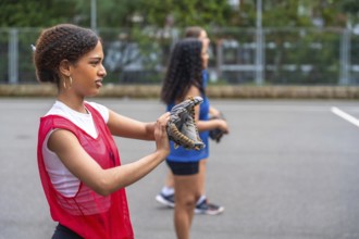 Young woman baseball player putting on her glove, preparing for practice with teammates under the