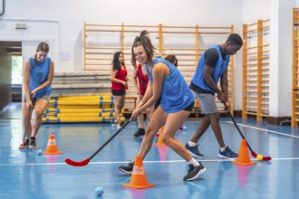 Female and male athletes wearing blue t shirts are practicing floorball, dribbling with sticks