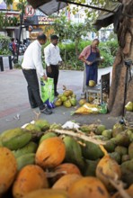Indian man cutting a coconut, others watching, Begaluru or Bangalore, Karnataka, India