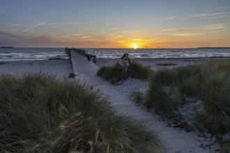 Sunset sky over the sea, wooden walkway and lifebuoy, framed by beach grass and calm water, Kobaek