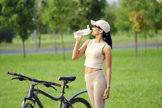 A woman dressed in activewear takes a refreshing drink from her water bottle while standing next to