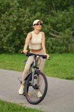 A woman enjoys a leisurely ride on her bicycle along a paved path in a vibrant green park. She