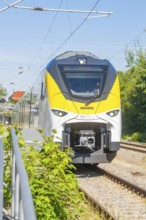 Train travelling on tracks under a clear sky, surrounded by green landscape, battery Electric train