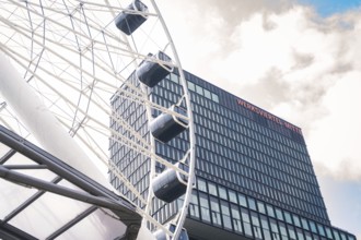 Large Ferris wheel next to a modern glass building under a cloudy sky, Werksviertel Munich, Munich,
