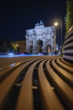 Siegestor at night with bench in the foreground and street lights, Siegestor, Munich, Germany