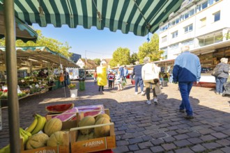 Visitors under striped market umbrellas stroll past a stall with melons and bananas, Sindelfingen,