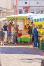 Vendors serving customers at an outdoor market stall with fresh fruit and vegetables, Sindelfingen,