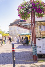 A hanging basket adorns the entrance to a city market full of relaxed people, Sindelfingen,