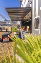A modern snack stand in a container, surrounded by plants, in sunny weather, Sindelfingen,