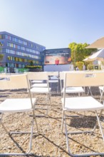 White chairs stand in rows in front of an outdoor screen on a sunny day, open air cinema