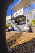 A sunny snack stand made from a container with barrels on a wooden chipboard floor, open air cinema