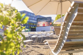 Rows of chairs under parasols in front of a screen, enlivened by sunshine, open air cinema