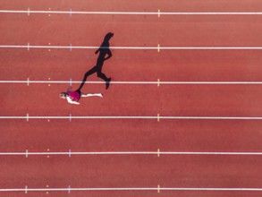 Aerial view of a female individual (runner) on a red athletics track (tartan track) with shadow as