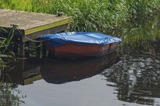 Red plastic boat with blue tarpaulin, Lower Saxony, Germany