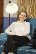 A woman sits comfortably on a vibrant blue couch, smiling while relaxing in a stylish living room