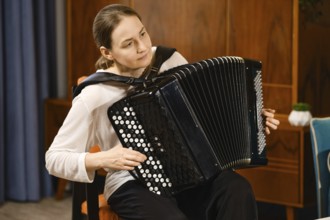A middle-aged woman concentrates as she plays the accordion in a warmly decorated room, creating a